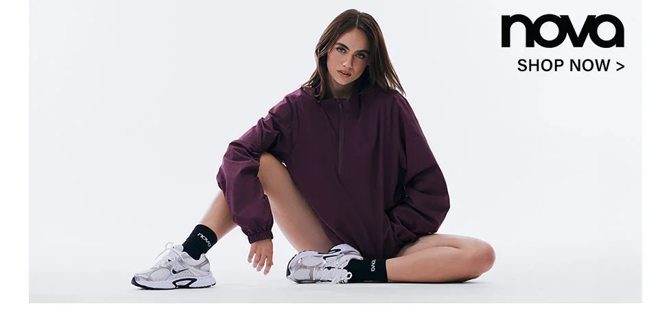 Woman wearing a burgundy oversized jacket, black Nova socks, and white sneakers, promoting stylish casual athletic wear. Shop the latest collection now.