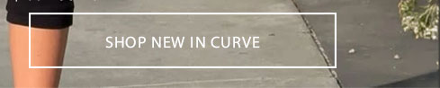Leg in black shorts against gray pavement with 'SHOP NEW IN CURVE' banner. Explore the latest curvy fashion arrivals.