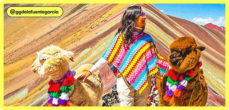 Image description: A woman wearing a colorful poncho stands between two alpacas, in front of Peru’s Rainbow Mountain.