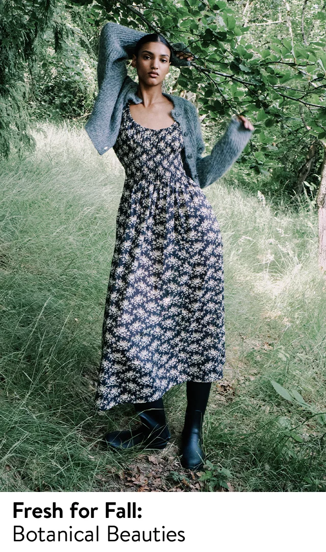 A woman wearing a long floral dress with black boots and a grey cardigan.