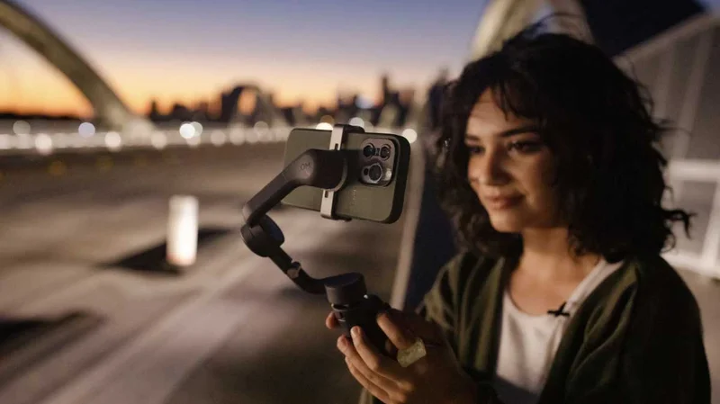 Image of woman holding gimbal with a phone on it standing on a bridge