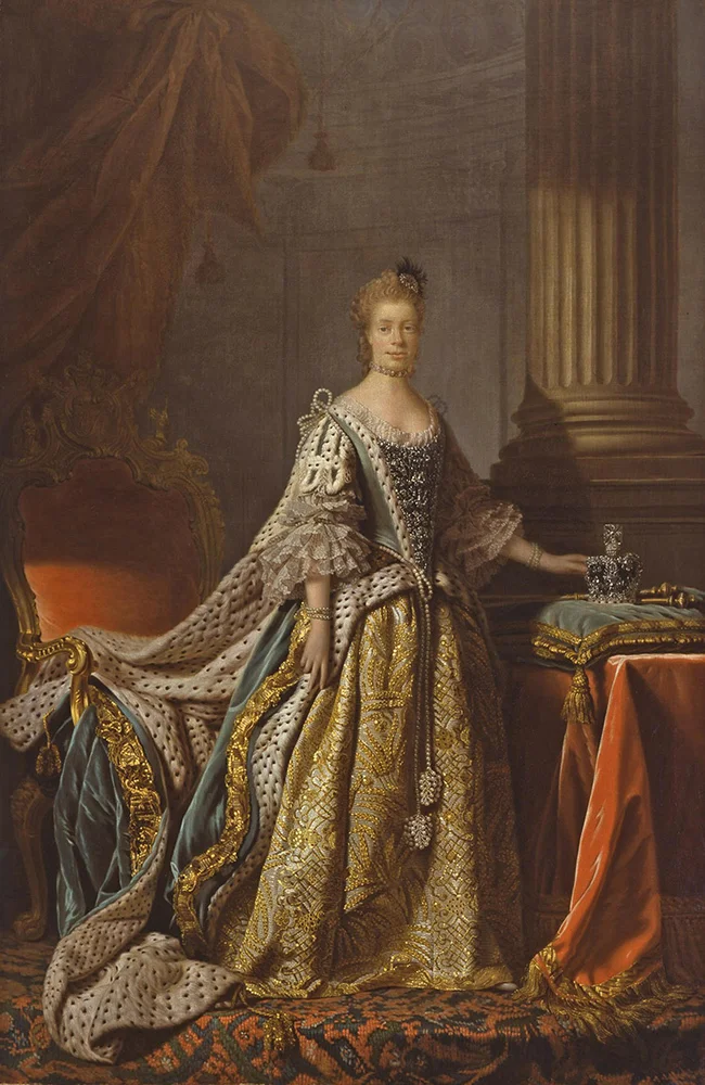 The queen stands, hand placed on crown, affixed on the viewer.