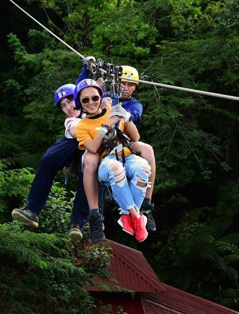 Image Description: Two female travelers zip lining through a lush forest in Costa Rica with a male guide