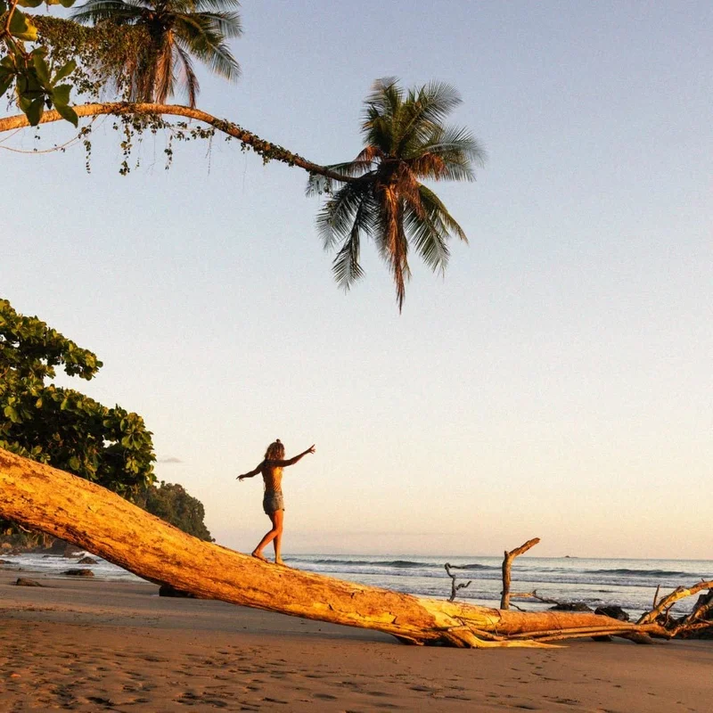 Image Description: A female traveler balancing on a log along a beach in Costa Rica