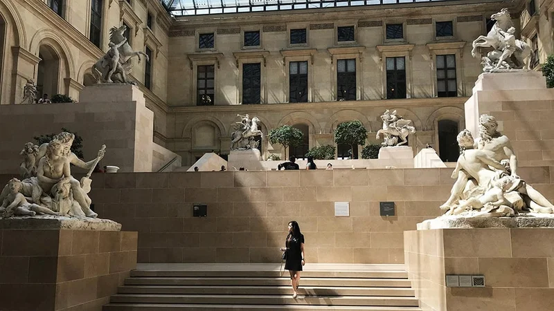 Image description: Woman walking down stairs at the Louvre, in Paris.