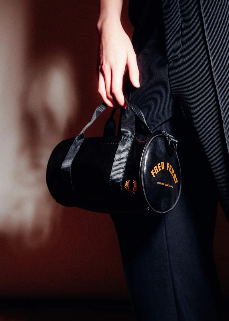 Close up of someone holding the Fred Perry Tonal Classic Mini Barrel Bag in Black / Gold