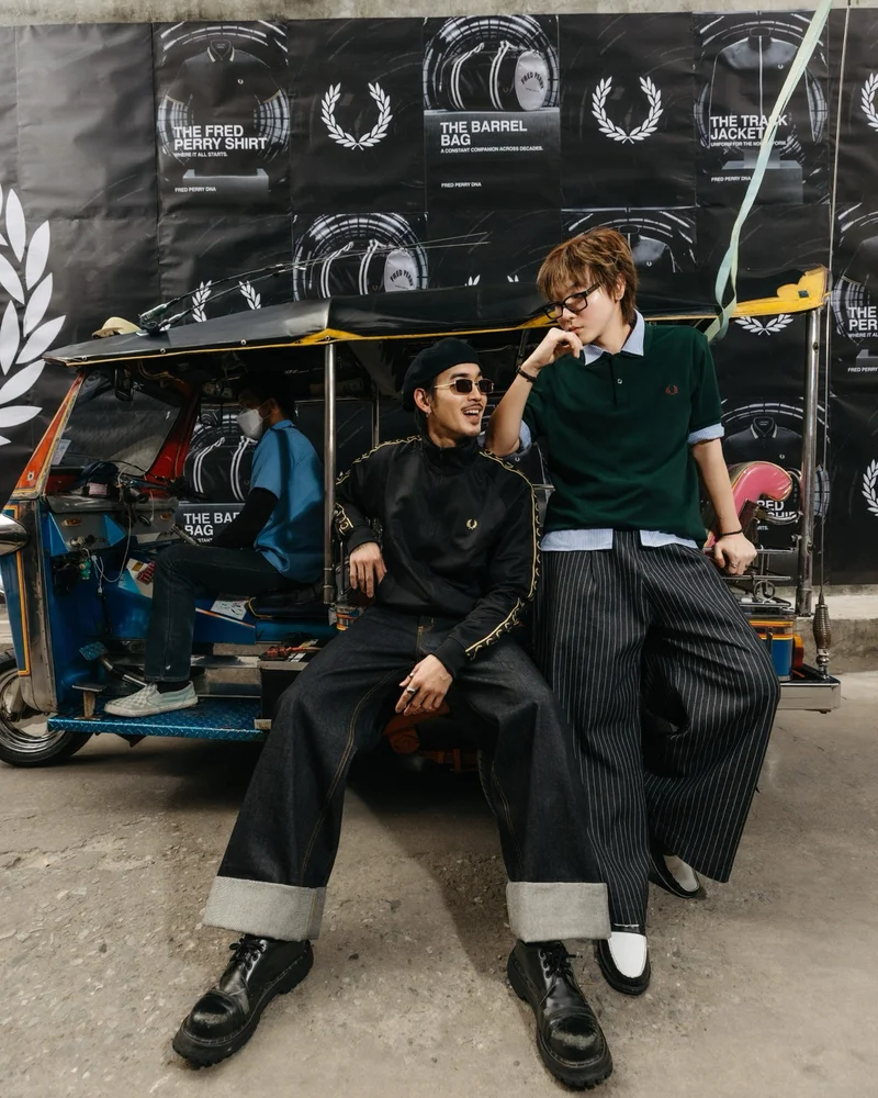Two male models wearing a Fred Perry Taped Track Jacket in Black / Champagne and Fred Perry Shirt in Green