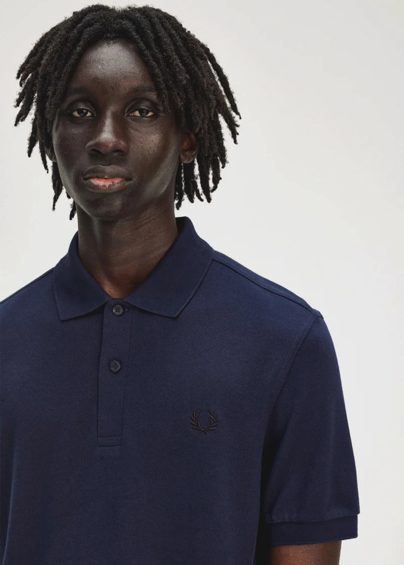Male Black model with locked hair wears a navy solid-colour Fred Perry polo shirt