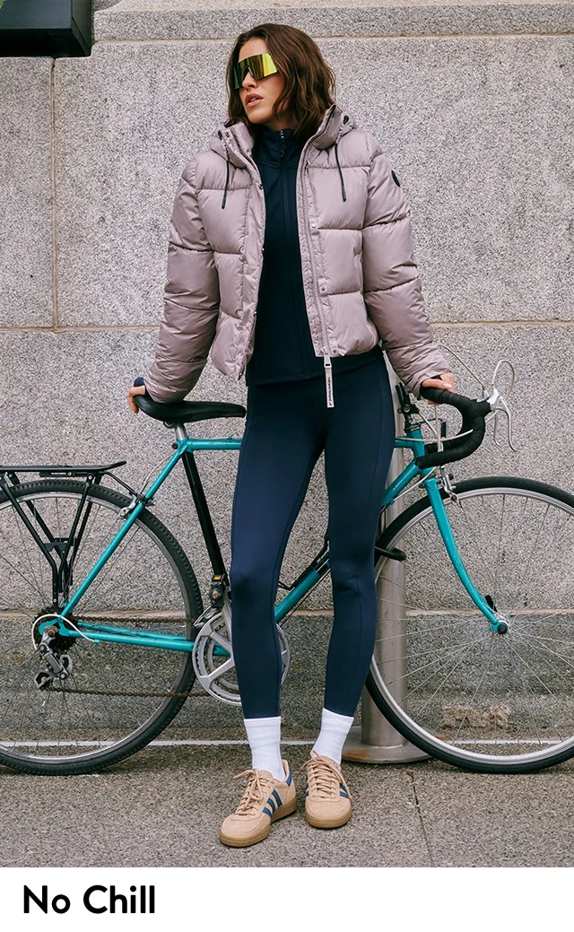 A woman wearing a puffer coat with sunglasses, leggings and sneakers.