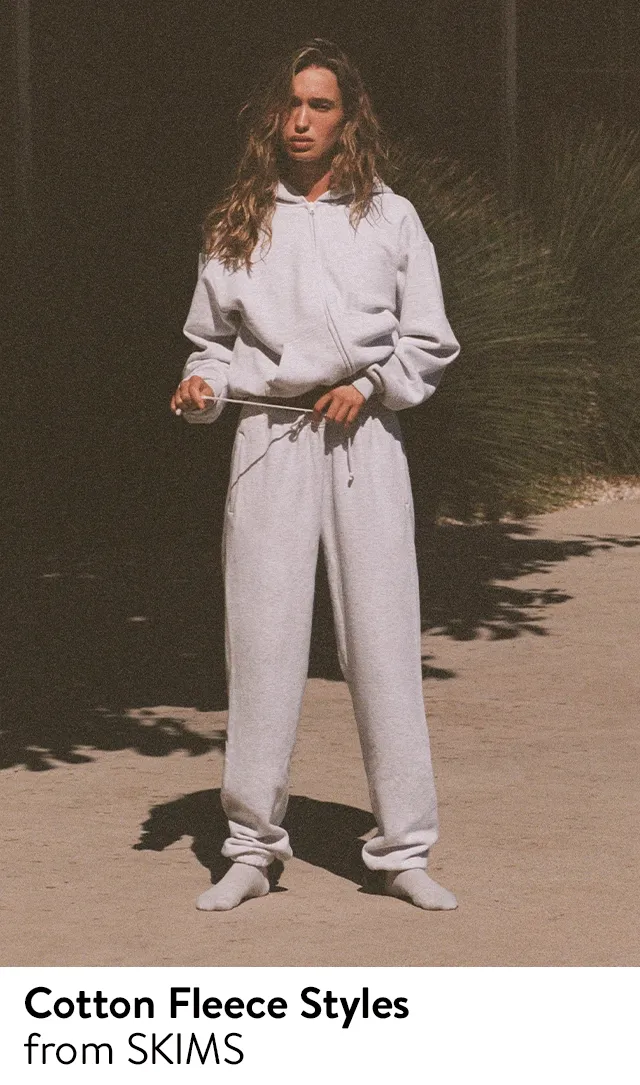 A woman wearing a grey hoodie and matching sweatpants from SKIMS.