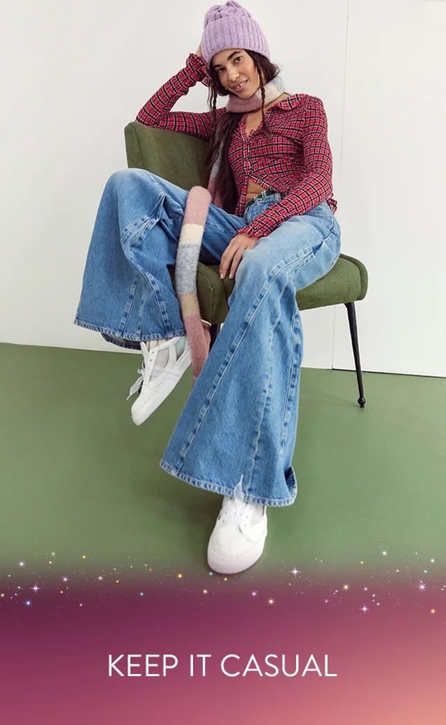 A young woman wearing a purple beanie, multicolored blouse and blue jeans.