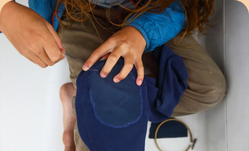 A young person sewing a patch onto a pair of pants.