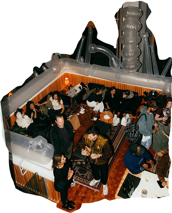 A lively scene at Ace Hotel Toronto with guests mingling in a room bordered by an artistic inflatable installation featuring abstract designs. Some attendees hold cocktails as they engage in conversation.