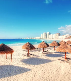 View of a beach in Cancun with natural, thatched umbrellas.