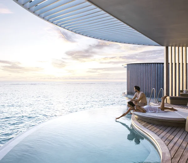 Couple in luxurious suite with private pool and view of the ocean. The woman is lying down, dipping her hand in the water.
