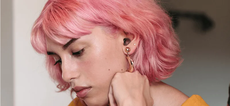 A pink-haired woman wearing Loop earplugs studies at a communal table.