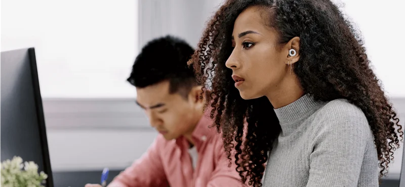 A woman wearing Loop earplugs works in an open-plan office.