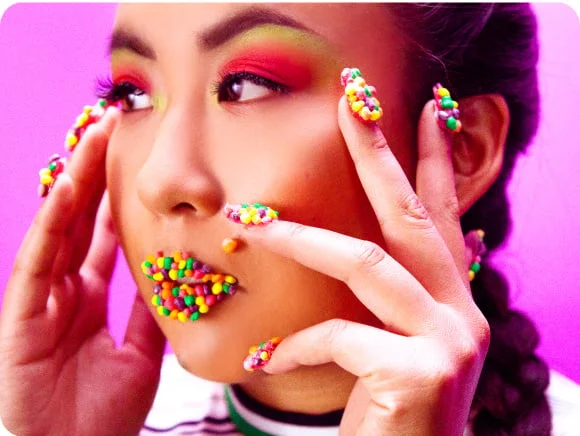 Model with bright colored eyeshadow and nerds candies on lips and fingernails
