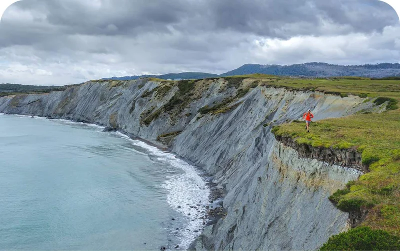 Patagonia Stories. A runner follows the edge of a gray cliff that drops into the sea.