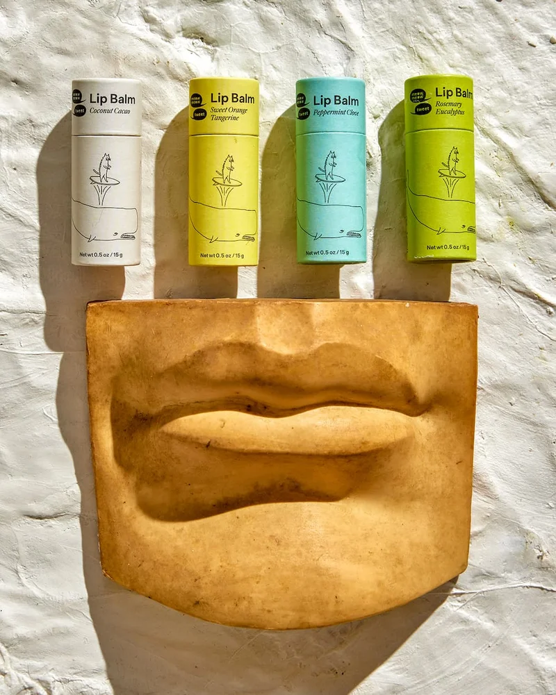 Four colorful lip balms are arranged atop a ceramic set of lips