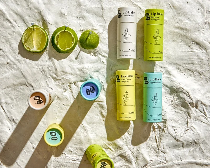 A collection of colorful lip balms is arranged on a plaster surface with pinned lime skins
