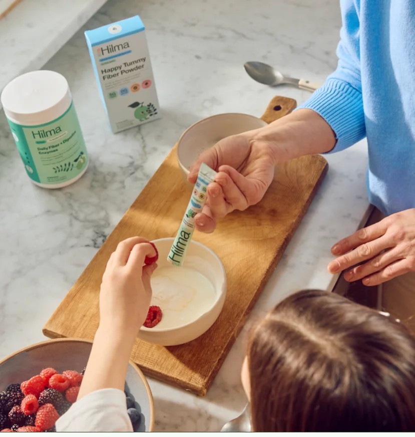Image of a mom and child pouring Happy Tummy Fiber Powder into yogurt