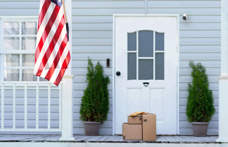 Front door of home with an American flag and multiple Arlo home security products are mounted on the exterior of the home.