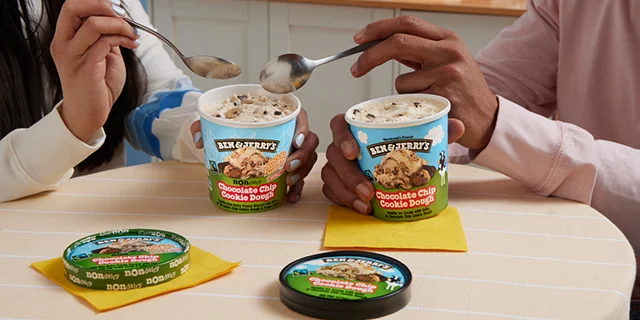 Two people sitting at a table, each eating a pint of Ben & Jerry's ice cream.