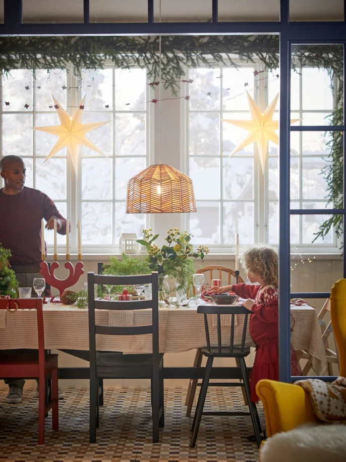 A man and child at a long table set up for a festive celebration with tableware, candles and plant decorations.