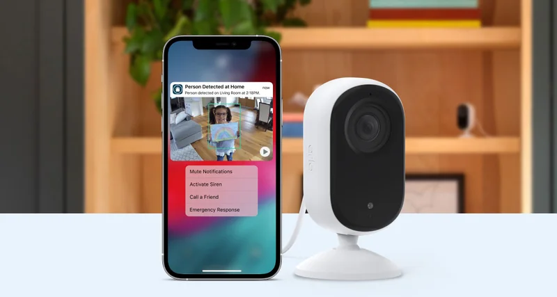 Arlo Essential 2K Indoor Camera next to a phone displaying a simulated screen image of an Arlo Secure notification with animated preview.