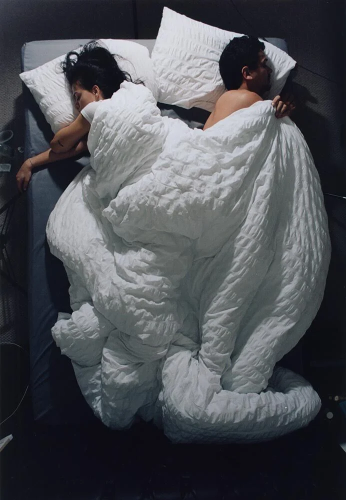 Two people face opposite directions in bed.
