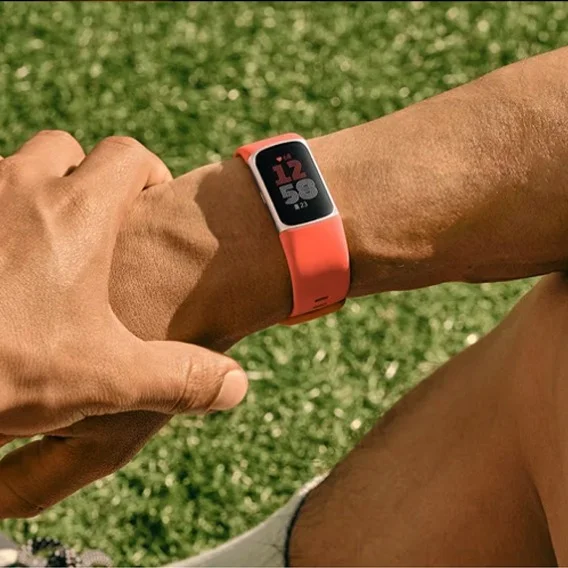 Photo of two hands against a backdrop of green grass. One hand is tapping on a Fitbit device on the other’s wrist.