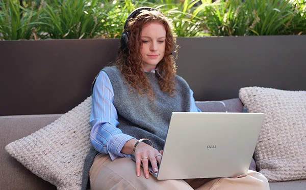 A woman sitting on an outdoor sofa with her Dell Pro Plus PB14250