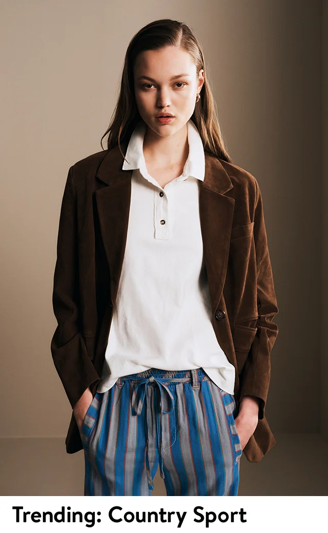 A woman wearing a white polo shirt, a brown blazer and striped pants.