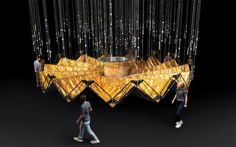 Several people circle around a half-scale prototype for a starshade, which looks like a folded golden structure.