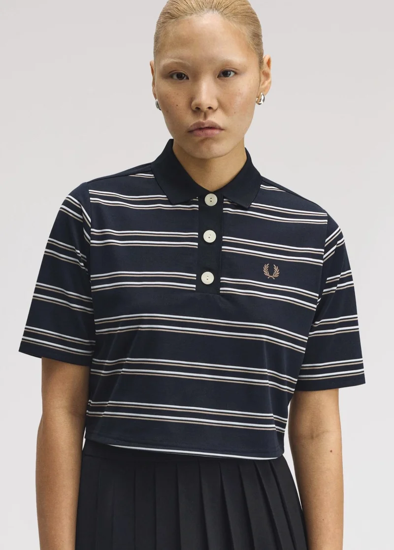 Female Asian model with slicked back bleached hair stares into the camera wearing a navy cropped boxy polo shirt with white stripes, a thick placket and statement white buttons