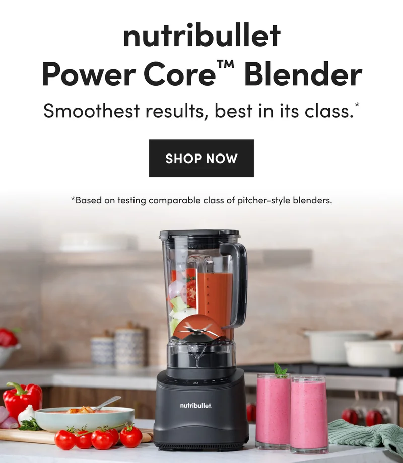 A black nutribullet blender filled with red sauce and vegetables, on a white counter next to two glasses of pink smoothie and a bowl of soup with fresh tomatoes.