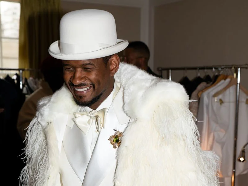 Image may contain: Usher, Clothing, Coat, Hat, Accessories, Formal Wear, Tie, Adult, Person, Suit, Jacket, Face, and Head