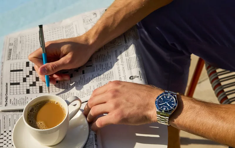 Person wearing the blue dial NJ0230-59L TSUYOSA Shore and playing a newspaper crossword game