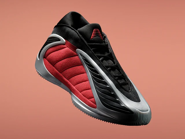 An black, grey and red adidas Anthony Edwards 2 basketball sneaker shown angled against a orange background. It has a sculpted sole and wave-like side design.