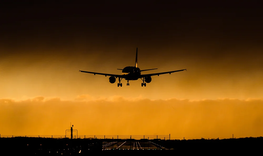 An airplane landing beneath a curtain of dark clouds; the plane is crooked in its approach due to the high winds