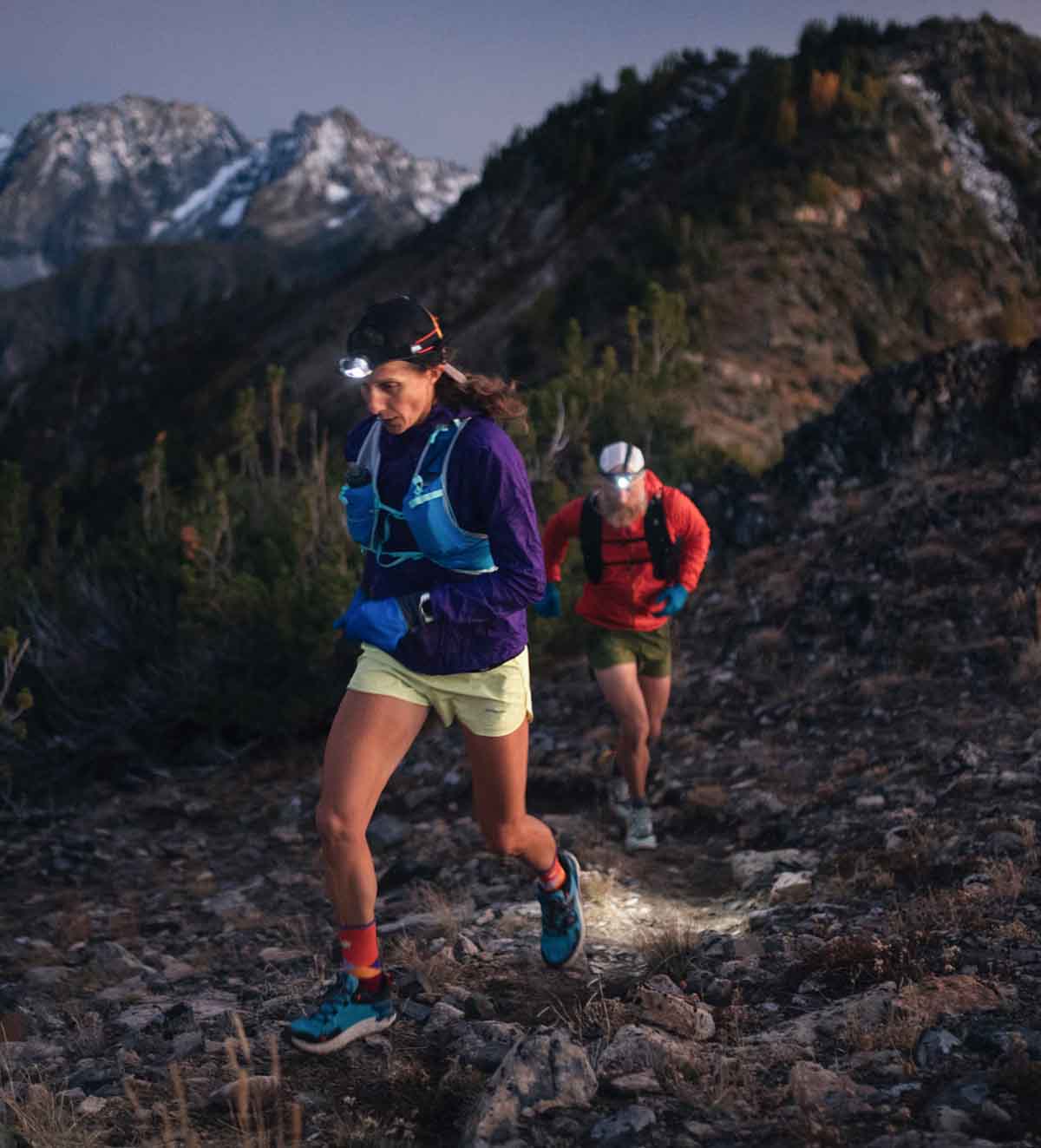 Two people running on a trail in the dark wearing  headlamps.