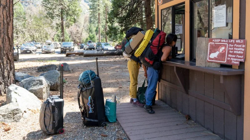 Two climbers stand at a ranger station in Yosemite with their luggage.