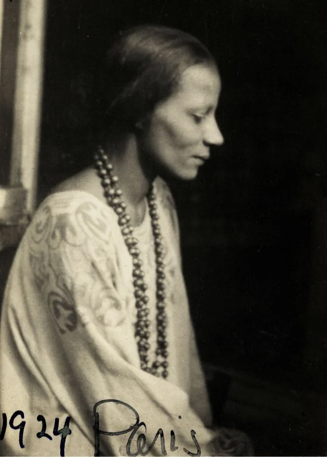 Black-and-white photograph of a woman in profile wearing a long necklace, inscribed “1924 Paris”