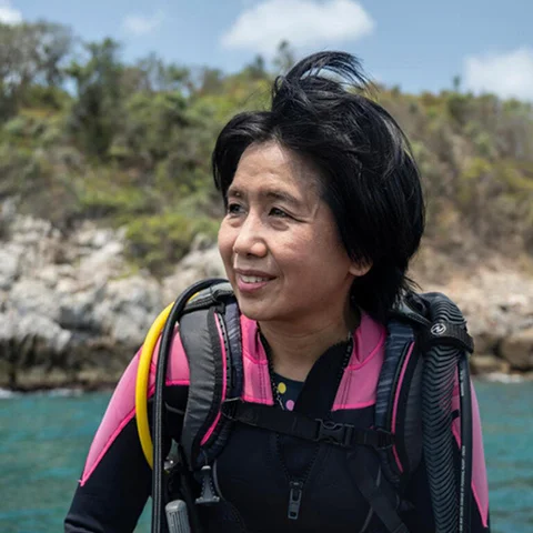 A woman in a pink and black wetsuit stands in the water, smiling at the camera.