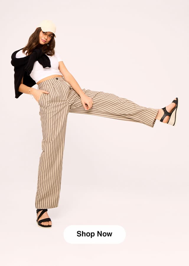 A woman kicking up her leg wearing a baseball cap, white tee, striped pants, and the Inca Espadrille Wedge Sandal in Black. Shop Now.