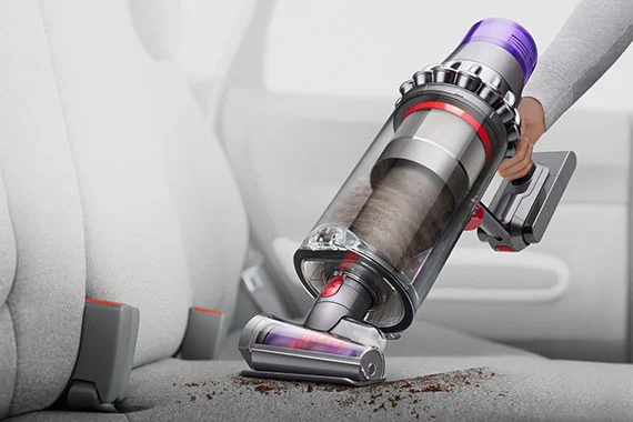 Person cleaning car seat with vacuum in hand-held mode