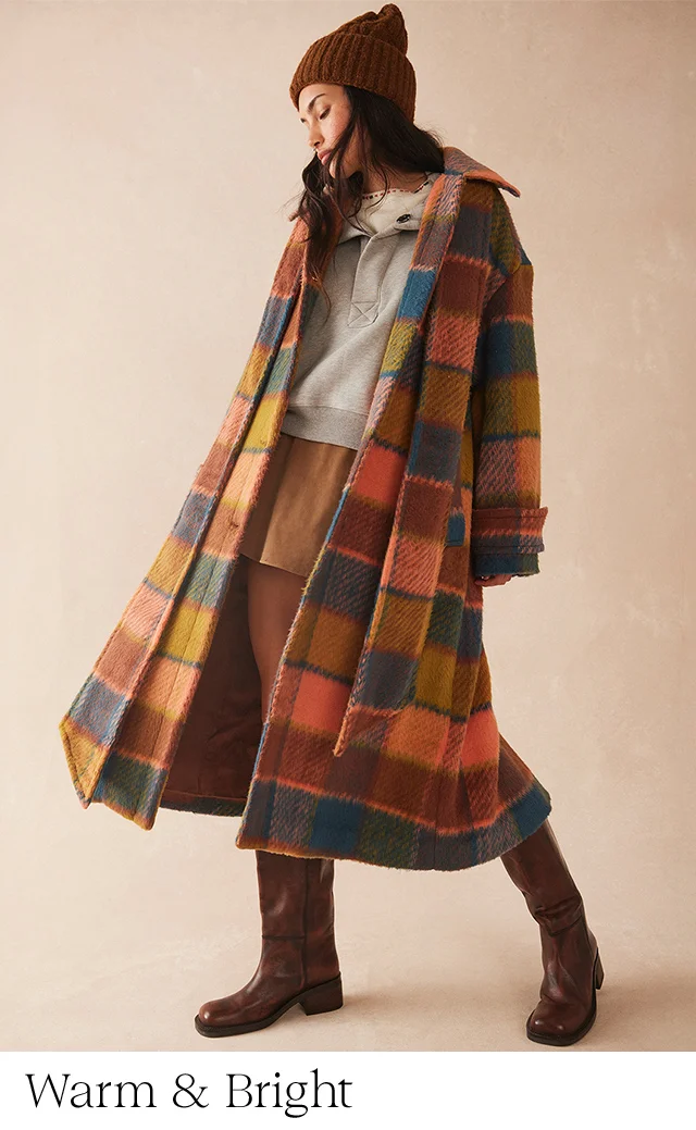 A woman wearing a plaid wool coat over a sweatshirt, skirt, boots and beanie.