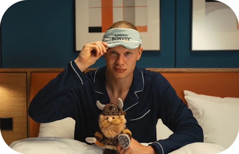 Soccer player Erling Haaland wearing a Marriott Bonvoy eye mask and holding a plush Viking toy.