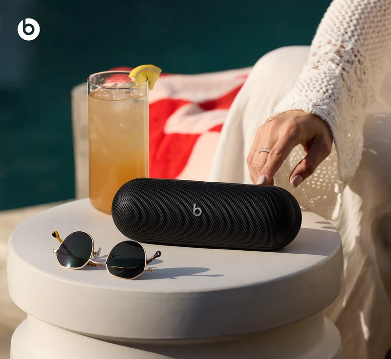 Beats Pill in Matte Black shown on a poolside table, sitting next to sunglasses and a cold drink.
